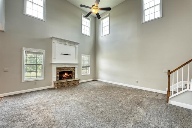 unfurnished living room featuring carpet flooring, a high ceiling, a stone fireplace, and ceiling fan