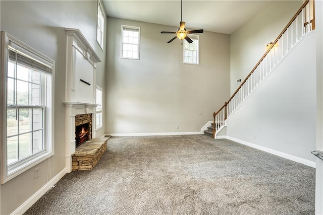 unfurnished living room featuring carpet, a wealth of natural light, a stone fireplace, and ceiling fan