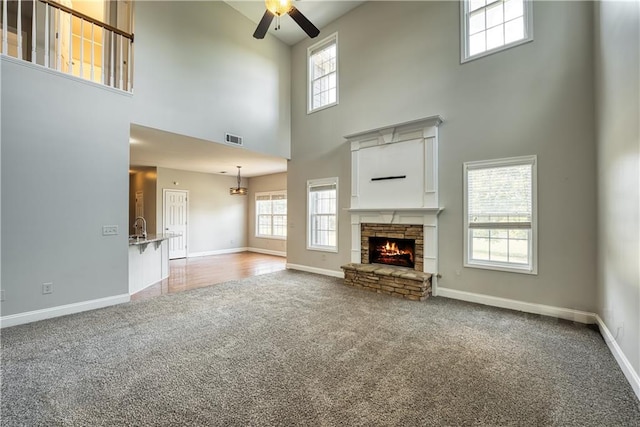 unfurnished living room with carpet, a towering ceiling, a stone fireplace, and ceiling fan