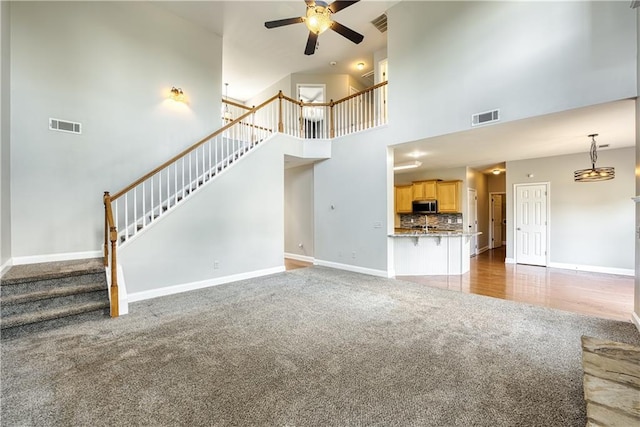 unfurnished living room featuring ceiling fan, carpet floors, and a high ceiling