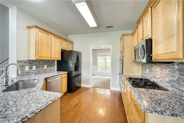 kitchen featuring light brown cabinetry, light stone counters, sink, and black appliances