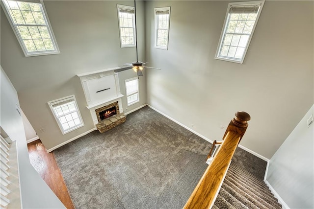 living room featuring ceiling fan, plenty of natural light, a fireplace, and a high ceiling