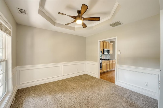 unfurnished room featuring a raised ceiling, ceiling fan, light colored carpet, and a healthy amount of sunlight