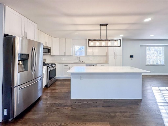 kitchen featuring pendant lighting, dark wood-type flooring, appliances with stainless steel finishes, white cabinetry, and a center island