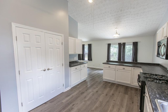 706 Hillmont Dr, Loganville, GA 30052 - kitchen with black gas range, dark countertops, stainless steel microwave, a textured ceiling, and white cabinetry