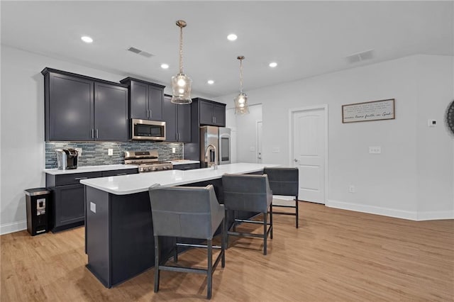 kitchen featuring hanging light fixtures, light hardwood / wood-style floors, a breakfast bar area, a kitchen island with sink, and appliances with stainless steel finishes