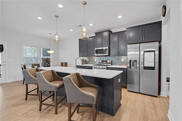 kitchen with a breakfast bar, appliances with stainless steel finishes, decorative light fixtures, and an island with sink