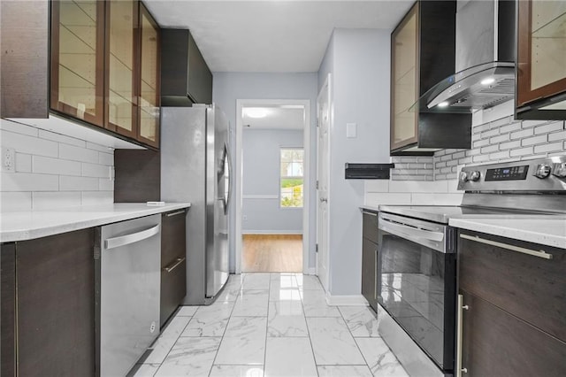 kitchen with marble finish floor, appliances with stainless steel finishes, wall chimney exhaust hood, light countertops, and baseboards