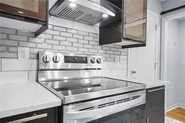 kitchen featuring backsplash, stainless steel electric range oven, baseboards, and extractor fan