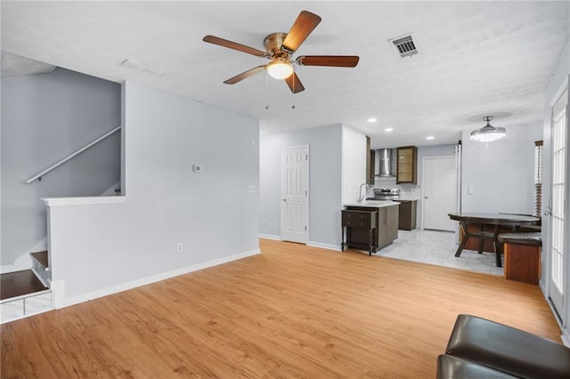 unfurnished living room with a ceiling fan, visible vents, light wood finished floors, a sink, and stairs