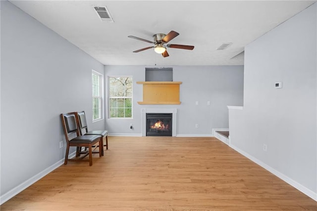 living area featuring a glass covered fireplace, ceiling fan, visible vents, and light wood-type flooring