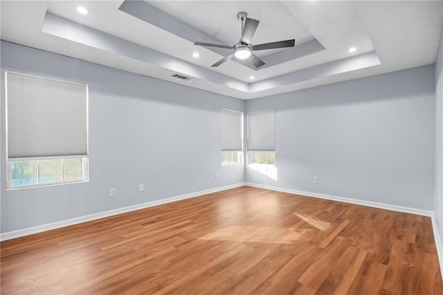 spare room with light wood-type flooring, visible vents, a raised ceiling, plenty of natural light, and baseboards