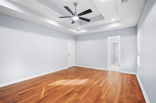 unfurnished room with a tray ceiling, baseboards, light wood-style flooring, and a ceiling fan