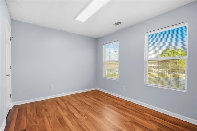 unfurnished room featuring wood finished floors, visible vents, and baseboards