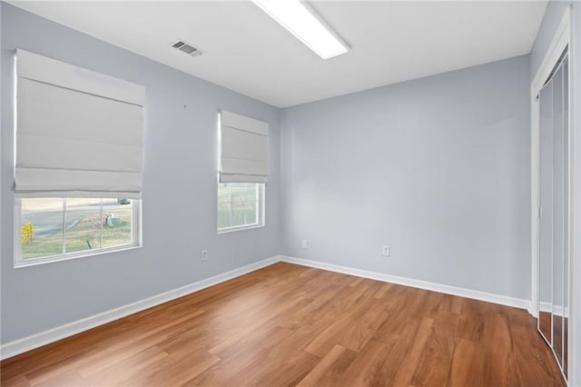 unfurnished room featuring wood finished floors, visible vents, and baseboards