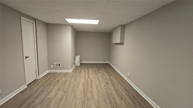 finished basement featuring a paneled ceiling, visible vents, baseboards, and wood finished floors