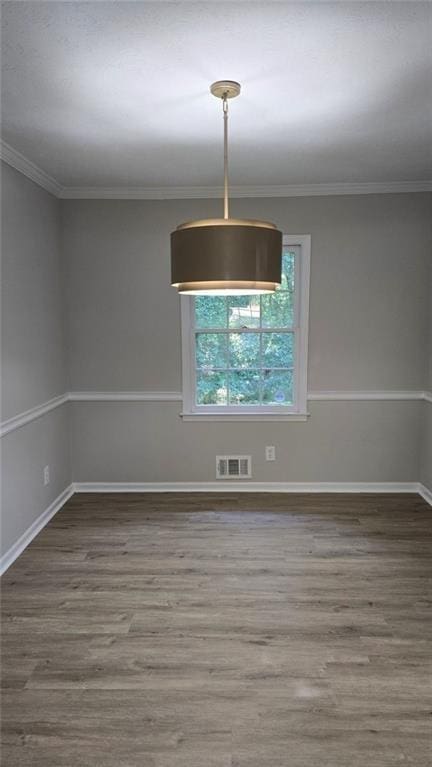 empty room featuring ornamental molding, wood finished floors, visible vents, and baseboards