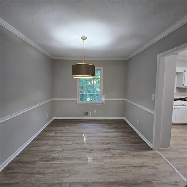 unfurnished dining area featuring baseboards, crown molding, visible vents, and wood finished floors