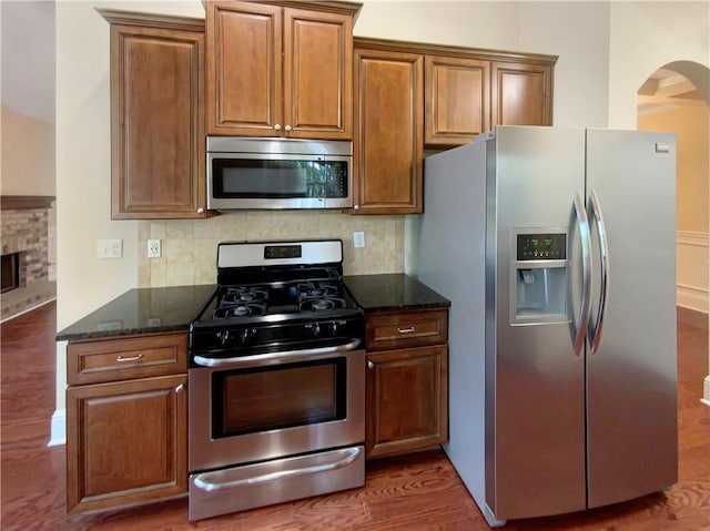 kitchen with appliances with stainless steel finishes, dark stone counters, dark hardwood / wood-style floors, a fireplace, and backsplash