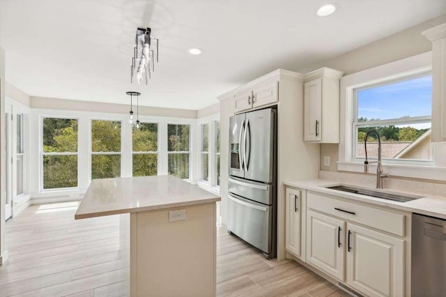 kitchen with sink, stainless steel appliances, white cabinets, a kitchen island, and decorative light fixtures