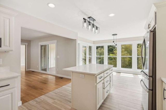 kitchen with white cabinetry, decorative light fixtures, a center island, light wood-type flooring, and stainless steel refrigerator