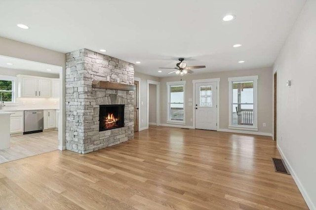 unfurnished living room featuring sink, a fireplace, ceiling fan, and light wood-type flooring