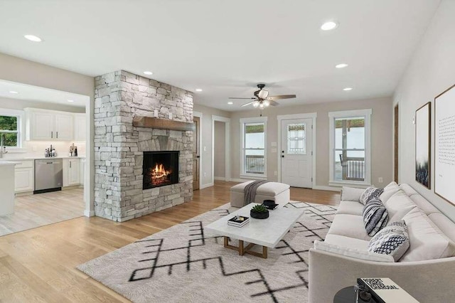 living room featuring ceiling fan, a stone fireplace, sink, and light wood-type flooring