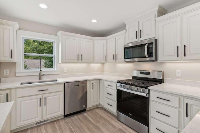 kitchen with white cabinetry, stainless steel appliances, sink, and light stone counters