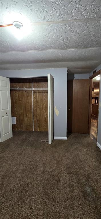 unfurnished bedroom with a textured ceiling, dark carpet, and a closet