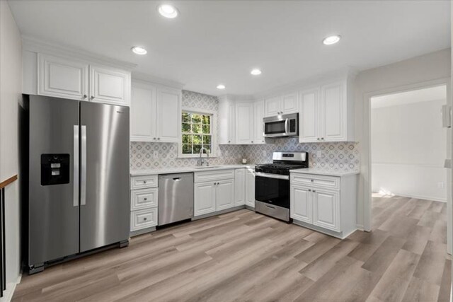 kitchen with white cabinets, decorative backsplash, light hardwood / wood-style floors, and appliances with stainless steel finishes