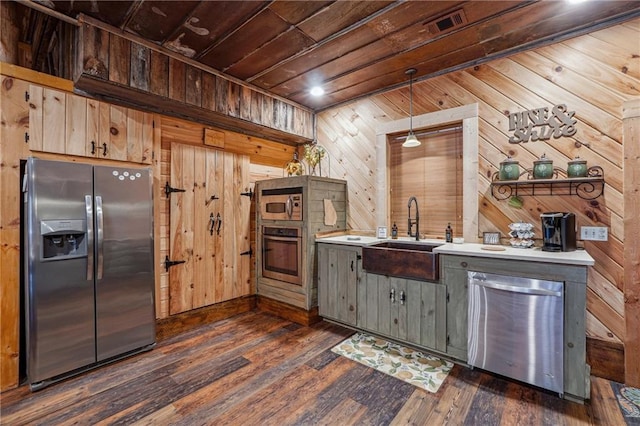 kitchen with sink, dark wood-type flooring, decorative light fixtures, wooden walls, and appliances with stainless steel finishes