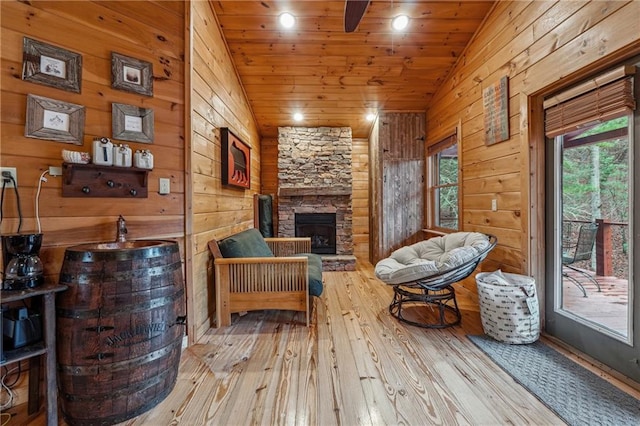 living area featuring wood walls, wooden ceiling, vaulted ceiling, a fireplace, and light hardwood / wood-style floors