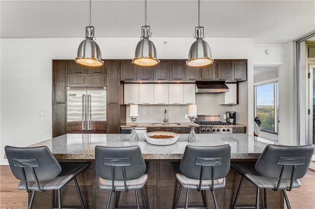 kitchen featuring light wood-type flooring, stainless steel appliances, a center island with sink, and decorative backsplash