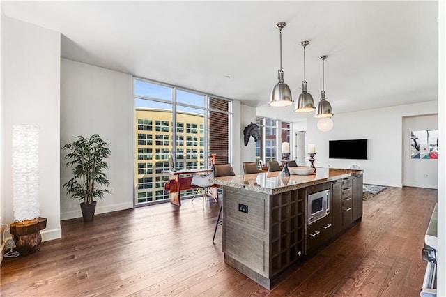 kitchen with a kitchen breakfast bar, hanging light fixtures, stainless steel microwave, a center island, and dark hardwood / wood-style flooring