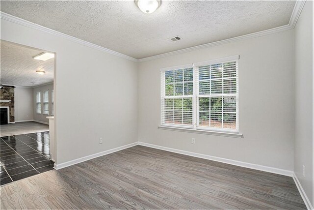 empty room featuring ornamental molding, a textured ceiling, dark wood-type flooring, and a stone fireplace