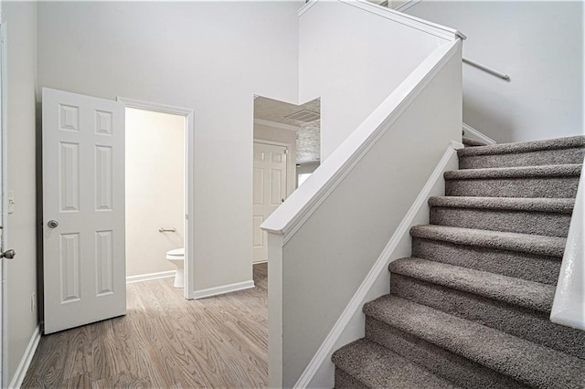 stairs featuring wood-type flooring, a high ceiling, and ornamental molding