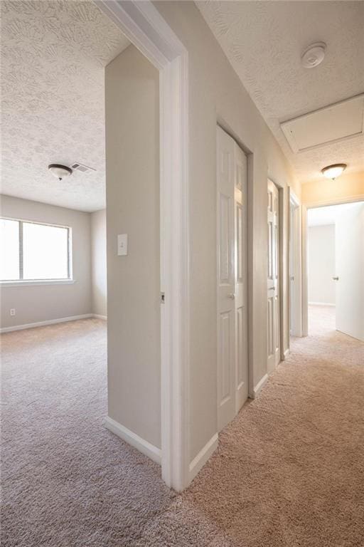 corridor featuring a textured ceiling, carpet, visible vents, and baseboards