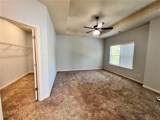 unfurnished bedroom with carpet, a closet, a raised ceiling, and ceiling fan