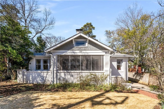 view of front of home featuring brick siding, a chimney, fence, and a sunroom