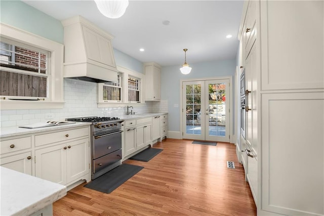 kitchen featuring light wood-style flooring, a sink, light countertops, custom exhaust hood, and decorative backsplash