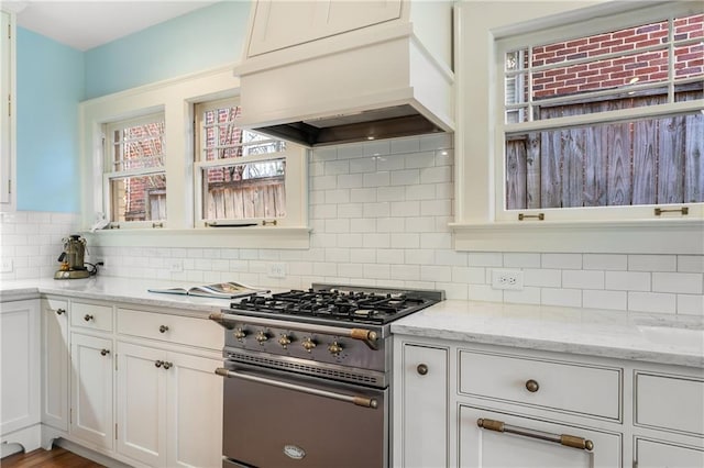 kitchen featuring premium range hood, white cabinets, decorative backsplash, high end range, and light stone countertops