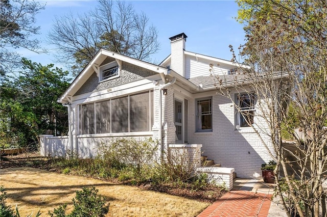 view of front of property with a sunroom, a chimney, and brick siding