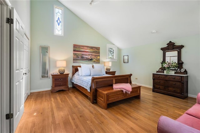 bedroom with high vaulted ceiling, light wood-type flooring, and baseboards