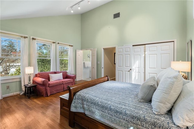 bedroom with a closet, rail lighting, visible vents, wood finished floors, and high vaulted ceiling