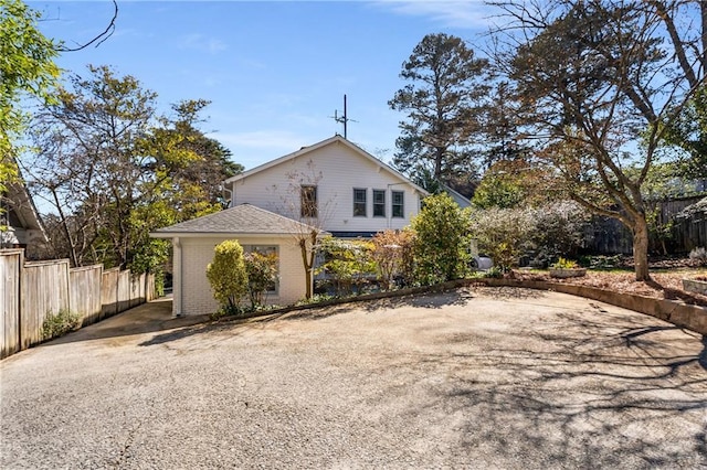 view of side of property featuring driveway, brick siding, and fence