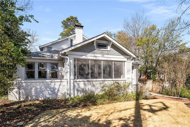 back of house with brick siding, a chimney, fence, and a sunroom