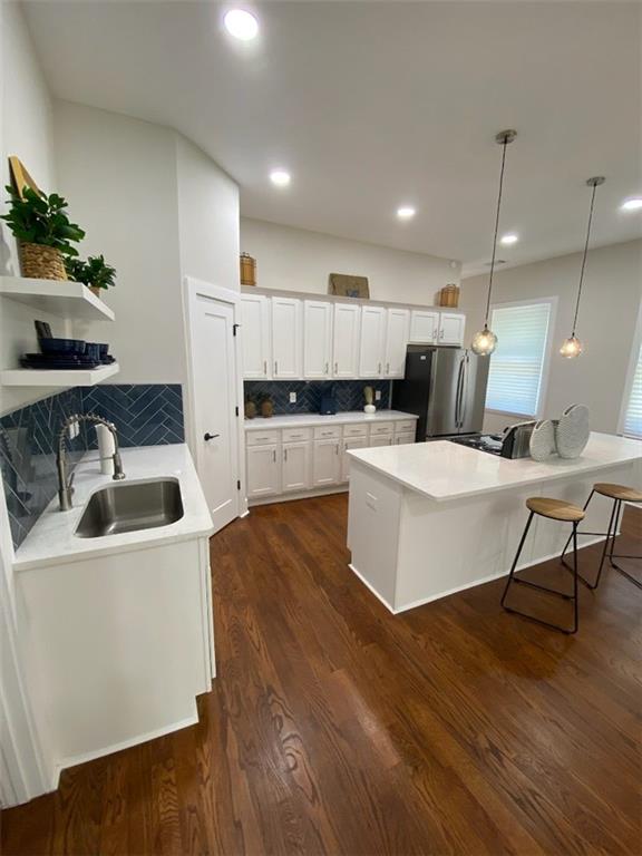 kitchen featuring white cabinets, decorative light fixtures, tasteful backsplash, sink, and stainless steel refrigerator