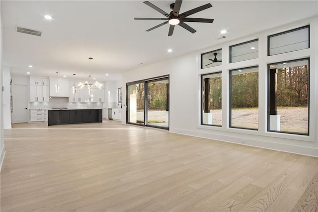 unfurnished living room with ceiling fan with notable chandelier, a wealth of natural light, and light hardwood / wood-style flooring