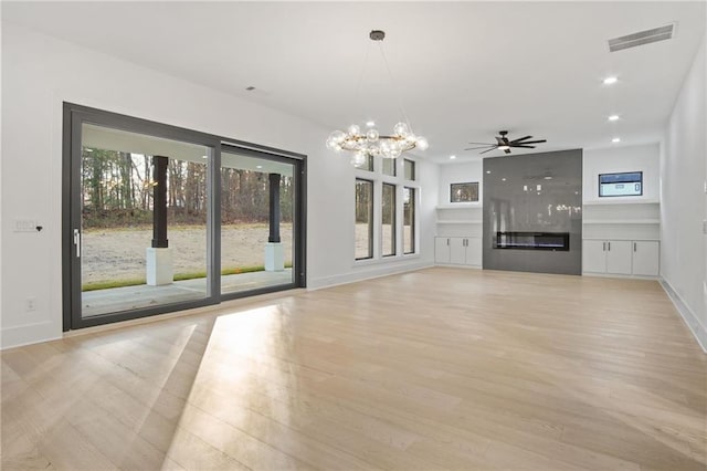 unfurnished living room with a high end fireplace, ceiling fan with notable chandelier, and light hardwood / wood-style flooring