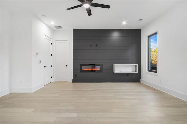 unfurnished living room with ceiling fan, light wood-type flooring, and a large fireplace